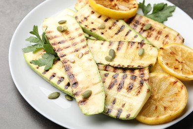 Photo of Delicious grilled courgette slices with pumpkin seeds, lemon and parsley on grey table, closeup