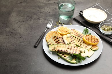 Photo of Delicious grilled courgette slices with pumpkin seeds, lemon and parsley on grey textured table, closeup