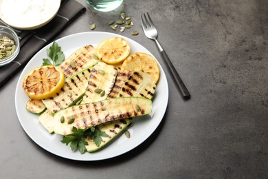 Photo of Delicious grilled courgette slices with pumpkin seeds, lemon and parsley on grey textured table, above view. Space for text