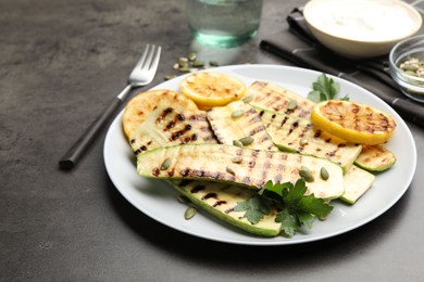 Photo of Delicious grilled courgette slices with pumpkin seeds, lemon and parsley on grey table, closeup