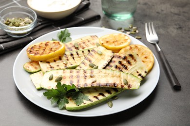 Photo of Delicious grilled courgette slices with pumpkin seeds, lemon and parsley on grey table, closeup