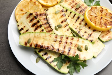 Photo of Delicious grilled courgette slices with pumpkin seeds, lemon and parsley on grey table, above view