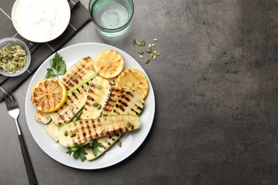 Photo of Delicious grilled courgette slices with pumpkin seeds, lemon and parsley served on grey textured table, flat lay. Space for text