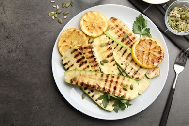Photo of Delicious grilled courgette slices with pumpkin seeds, lemon and parsley served on grey textured table, flat lay