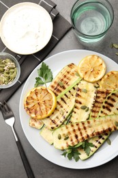 Photo of Delicious grilled courgette slices with pumpkin seeds, lemon and parsley served on grey textured table, flat lay