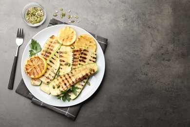 Photo of Delicious grilled courgette slices with pumpkin seeds, lemon and parsley served on grey textured table, flat lay. Space for text