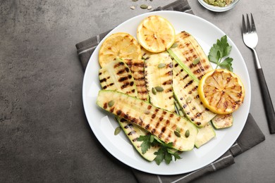 Photo of Delicious grilled courgette slices with pumpkin seeds, lemon and parsley served on grey textured table, flat lay. Space for text