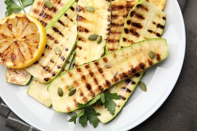 Photo of Delicious grilled courgette slices with pumpkin seeds, lemon and parsley on grey table, top view