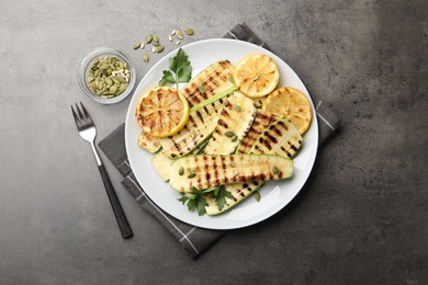 Photo of Delicious grilled courgette slices with pumpkin seeds, lemon and parsley served on grey textured table, flat lay
