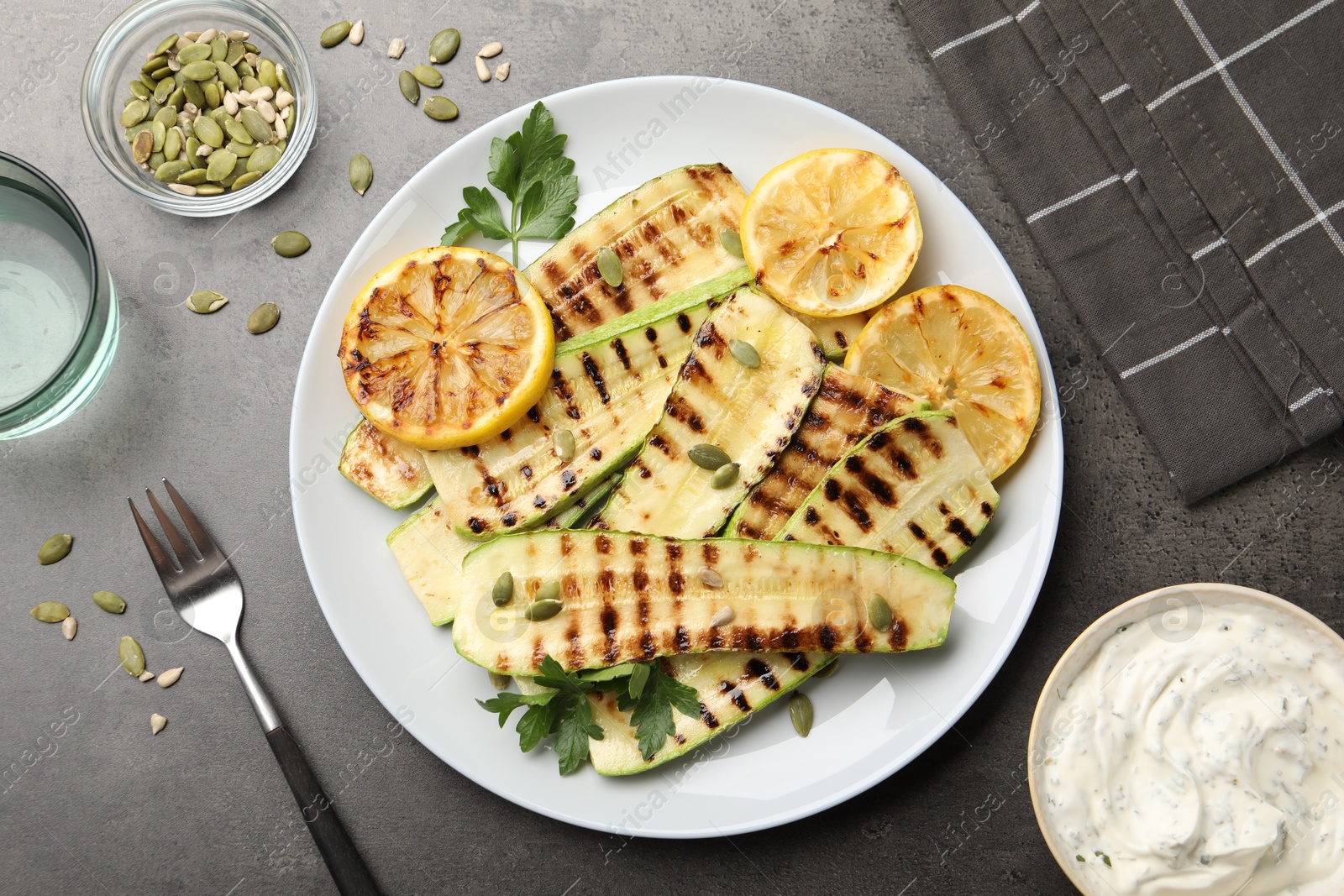 Delicious grilled courgette slices with pumpkin seeds, lemon and parsley served on grey textured table, flat lay Photo of Delicious grilled courgette slices with pumpkin seeds, lemon and parsley served on grey textured table, flat lay