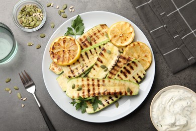 Photo of Delicious grilled courgette slices with pumpkin seeds, lemon and parsley served on grey textured table, flat lay