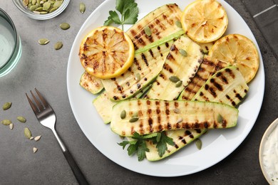 Photo of Delicious grilled courgette slices with pumpkin seeds, lemon and parsley served on grey textured table, flat lay