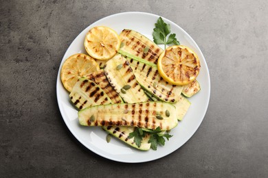 Photo of Delicious grilled courgette slices with pumpkin seeds, lemon and parsley on grey textured table, top view