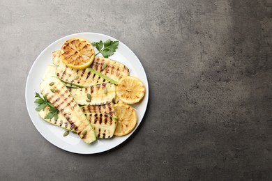 Photo of Delicious grilled courgette slices with pumpkin seeds, lemon and parsley on grey textured table, top view. Space for text