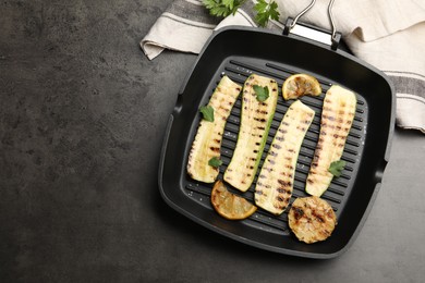 Photo of Delicious grilled courgette slices with garlic, lemon and parsley in pan on grey textured table, flat lay. Space for text
