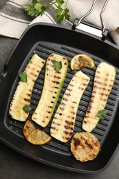 Photo of Delicious grilled courgette slices with garlic, lemon and parsley in pan on grey textured table, flat lay
