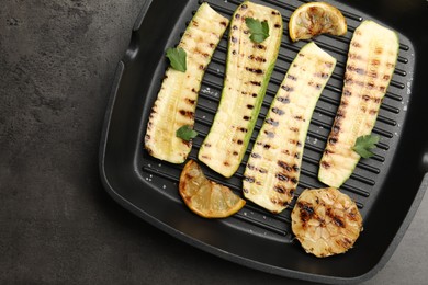Photo of Delicious grilled courgette slices with garlic, lemon and parsley in pan on grey textured table, top view