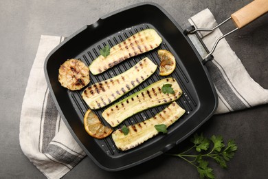 Photo of Delicious grilled courgette slices with garlic, lemon and parsley in pan on grey textured table, flat lay