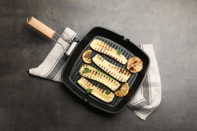 Photo of Delicious grilled courgette slices with garlic, lemon and parsley in pan on grey textured table, top view