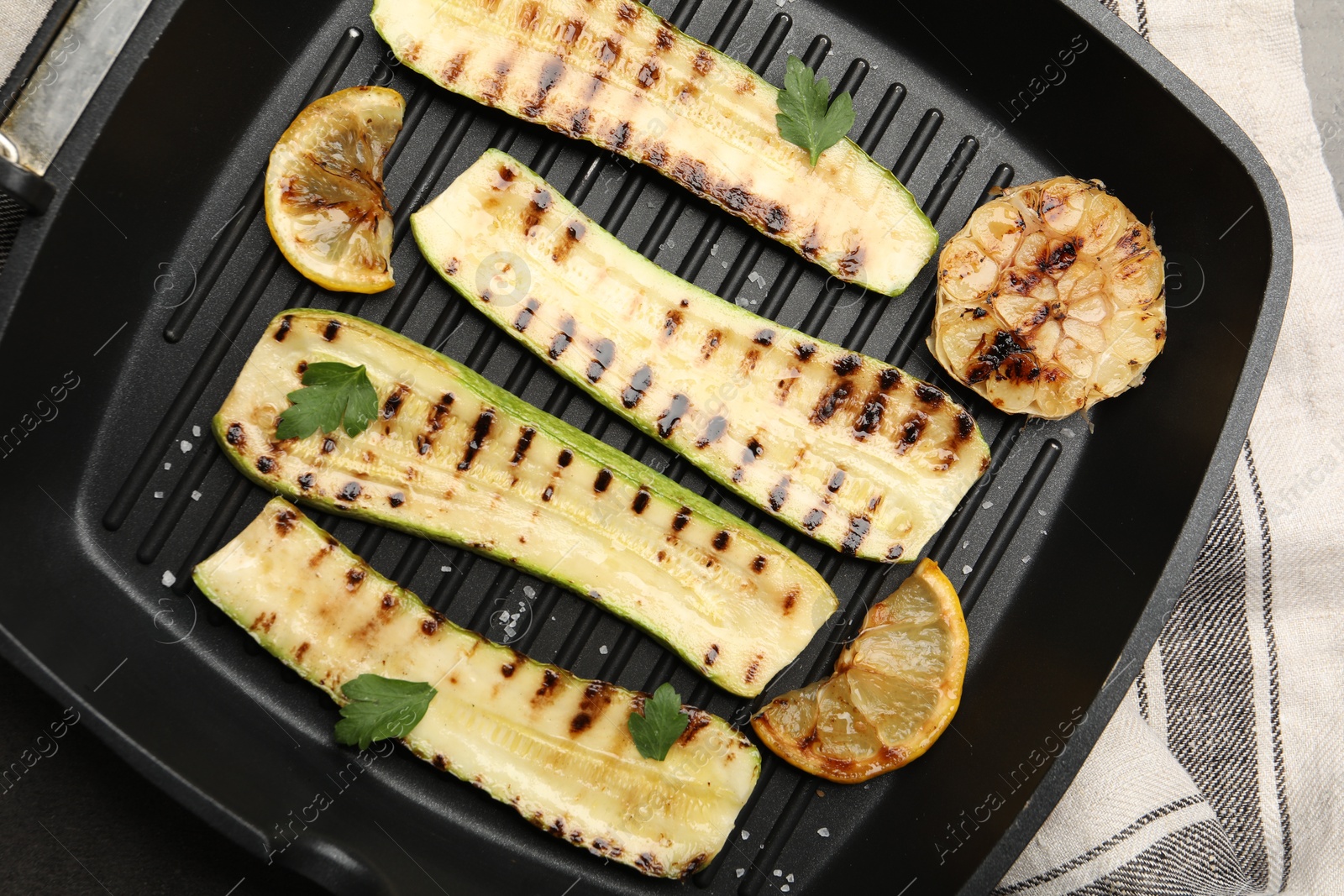 Photo of Delicious grilled courgette slices with garlic, lemon and parsley in pan on table, top view