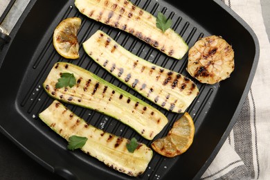 Photo of Delicious grilled courgette slices with garlic, lemon and parsley in pan on table, top view
