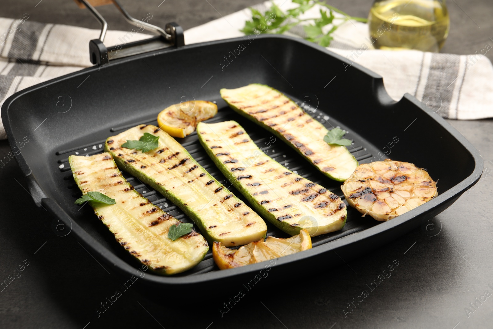 Photo of Delicious grilled courgette slices with garlic, lemon and parsley in pan on grey table, closeup
