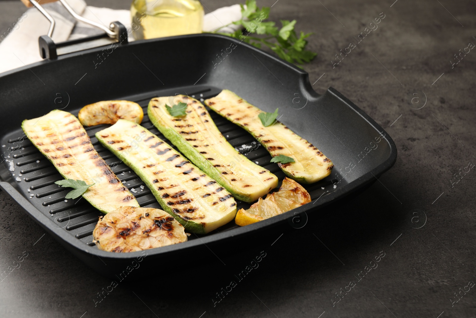 Photo of Delicious grilled courgette slices with garlic, lemon and parsley in pan on grey table, closeup