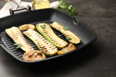 Photo of Delicious grilled courgette slices with garlic, lemon and parsley in pan on grey table, closeup