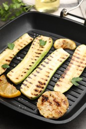 Photo of Delicious grilled courgette slices with garlic, lemon and parsley in pan on grey table, closeup