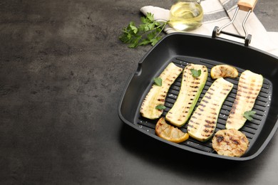 Photo of Delicious grilled courgette slices with garlic, lemon and parsley in pan on grey textured table, closeup. Space for text