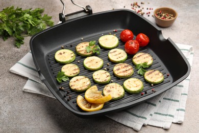 Photo of Delicious grilled courgette slices with tomatoes, lemon and parsley in pan on grey textured table, closeup