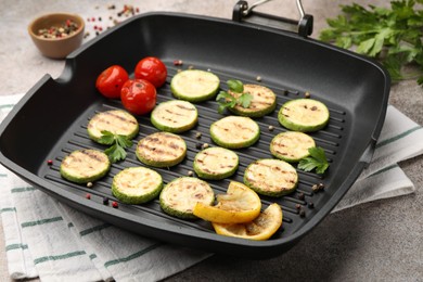 Photo of Delicious grilled courgette slices with tomatoes, lemon and parsley in pan on grey textured table, closeup