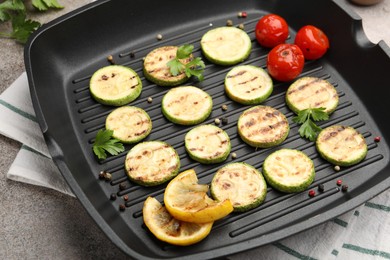 Photo of Delicious grilled courgette slices with tomatoes, lemon and parsley in pan on grey textured table, closeup