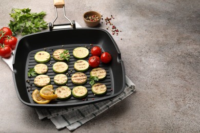 Photo of Delicious grilled courgette slices with tomatoes, lemon and parsley in pan on grey textured table, closeup. Space for text