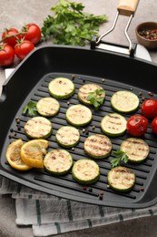 Photo of Delicious grilled courgette slices with tomatoes, lemon and parsley in pan on grey textured table, closeup