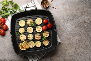 Photo of Delicious grilled courgette slices with tomatoes, lemon and parsley in pan on grey textured table, flat lay. Space for text