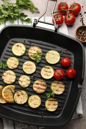Photo of Delicious grilled courgette slices with tomatoes, lemon and parsley in pan on grey textured table, flat lay