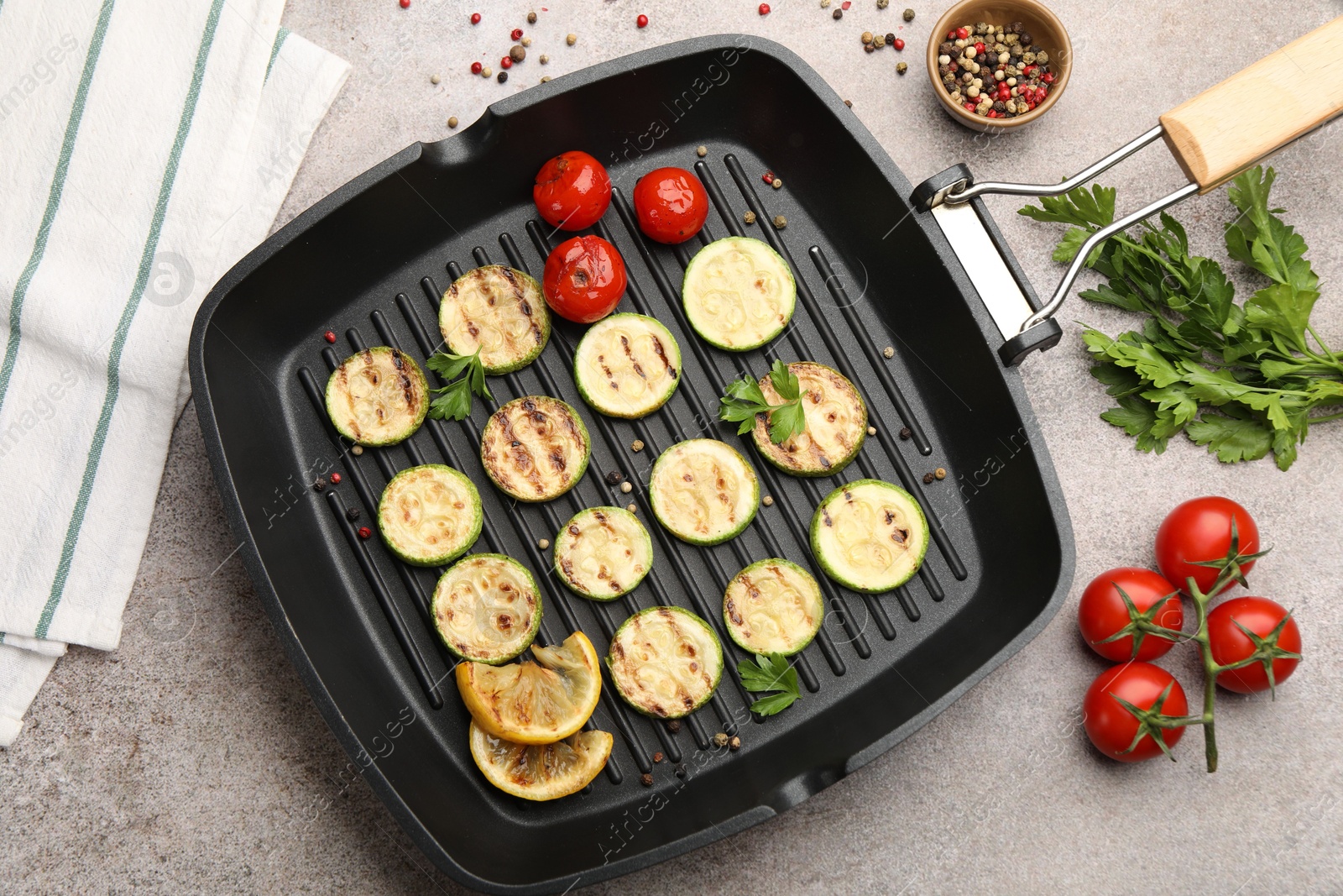 Delicious grilled courgette slices with tomatoes, lemon and parsley in pan on grey textured table, flat lay Photo of Delicious grilled courgette slices with tomatoes, lemon and parsley in pan on grey textured table, flat lay