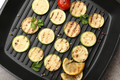 Photo of Delicious grilled courgette slices with tomatoes, lemon and parsley in pan on grey textured table, top view