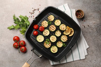 Photo of Delicious grilled courgette slices with tomatoes, lemon and parsley in pan on grey textured table, flat lay