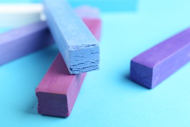 Photo of Colorful chalk pastels on light blue background, closeup