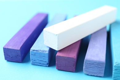 Photo of Colorful chalk pastels on light blue background, closeup