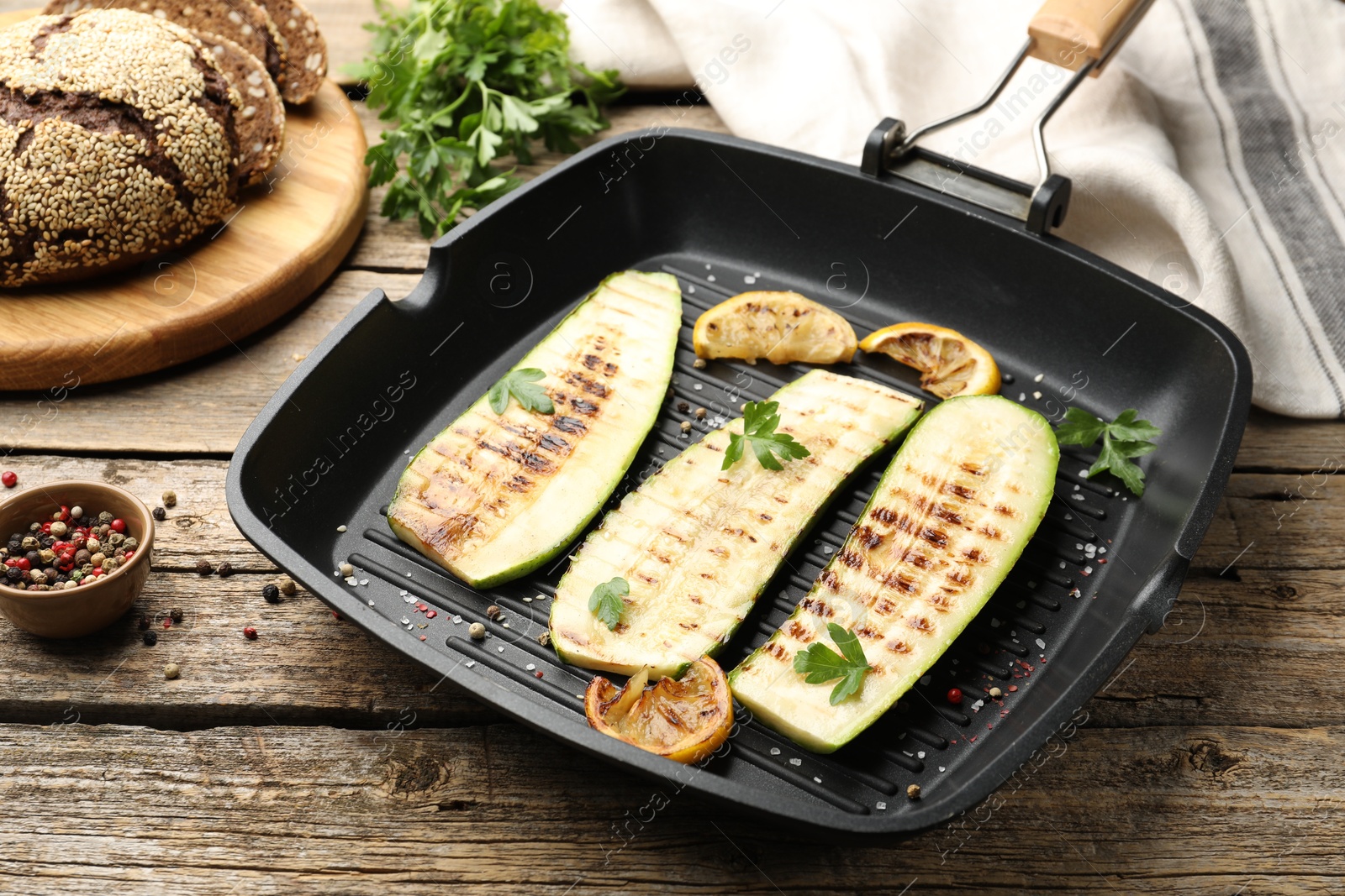 Photo of Delicious grilled courgette slices with spices and lemon in pan on wooden table, closeup