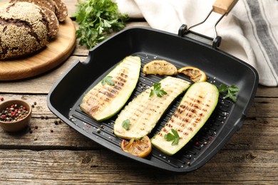 Photo of Delicious grilled courgette slices with spices and lemon in pan on wooden table, closeup