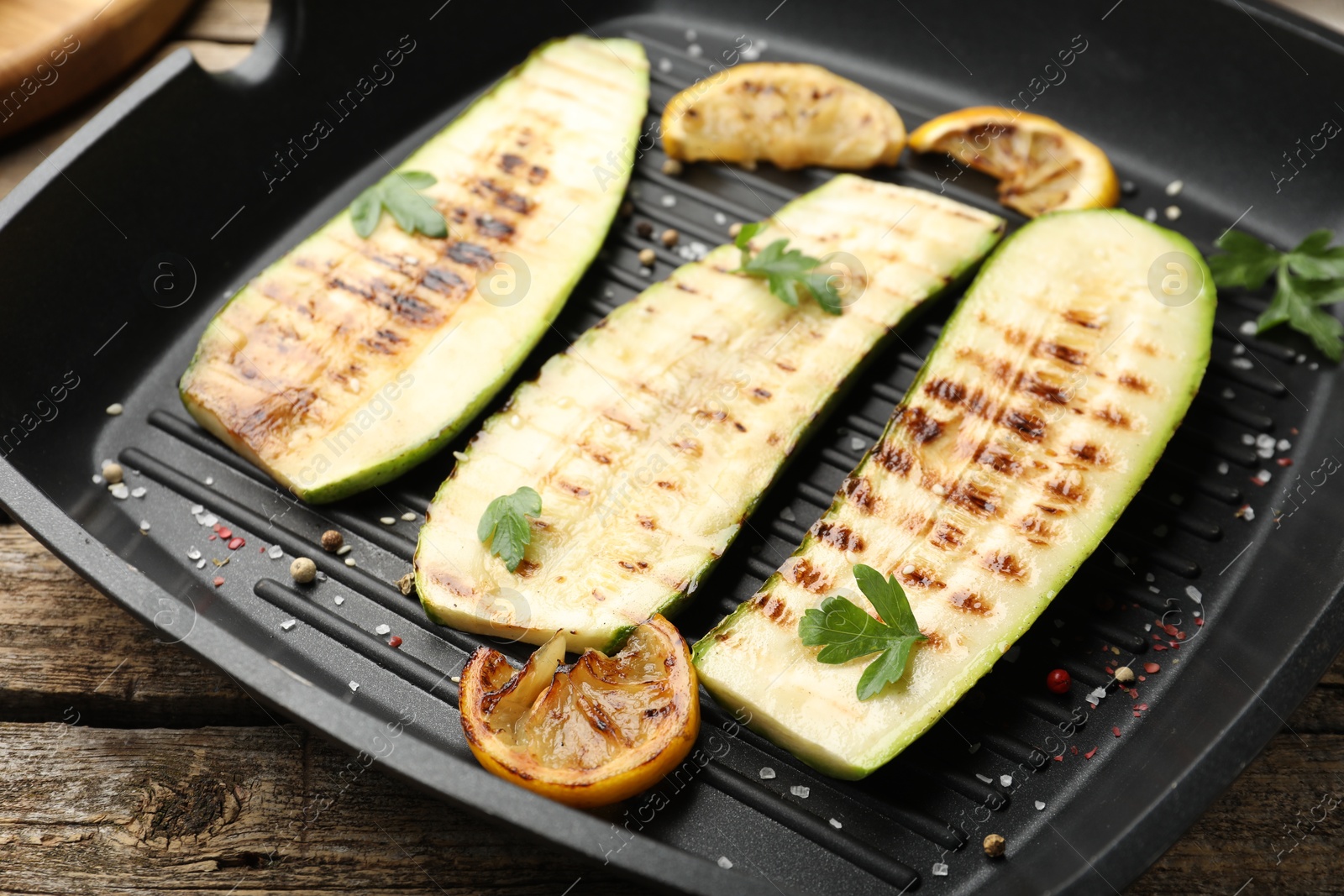 Photo of Delicious grilled courgette slices with spices and lemon in pan on wooden table, closeup