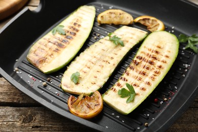 Photo of Delicious grilled courgette slices with spices and lemon in pan on wooden table, closeup
