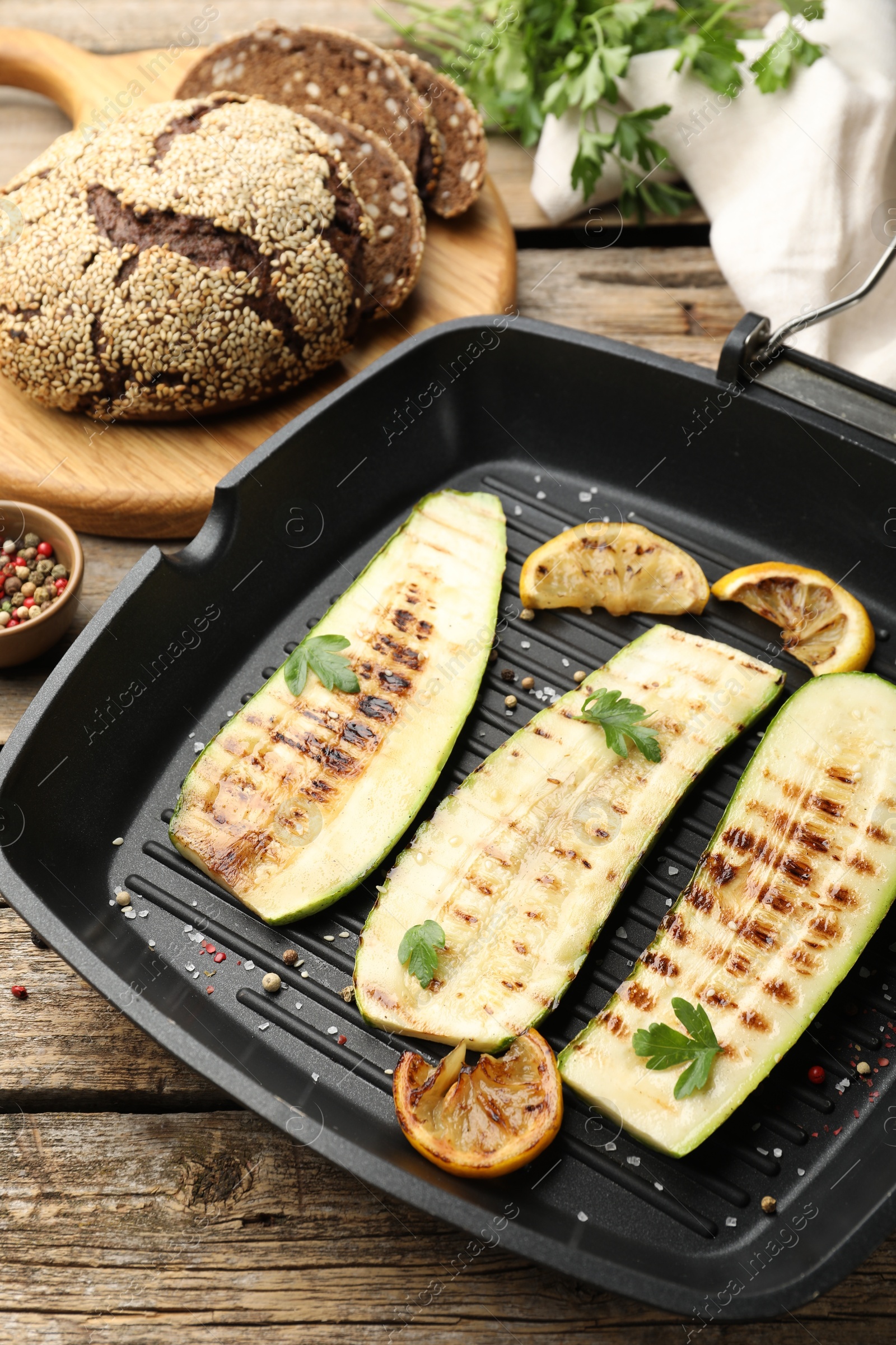 Photo of Delicious grilled courgette slices with spices and lemon in pan on wooden table, closeup