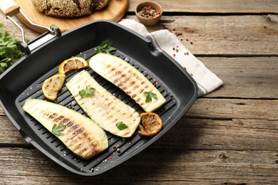 Photo of Delicious grilled courgette slices with spices and lemon in pan on wooden table, closeup