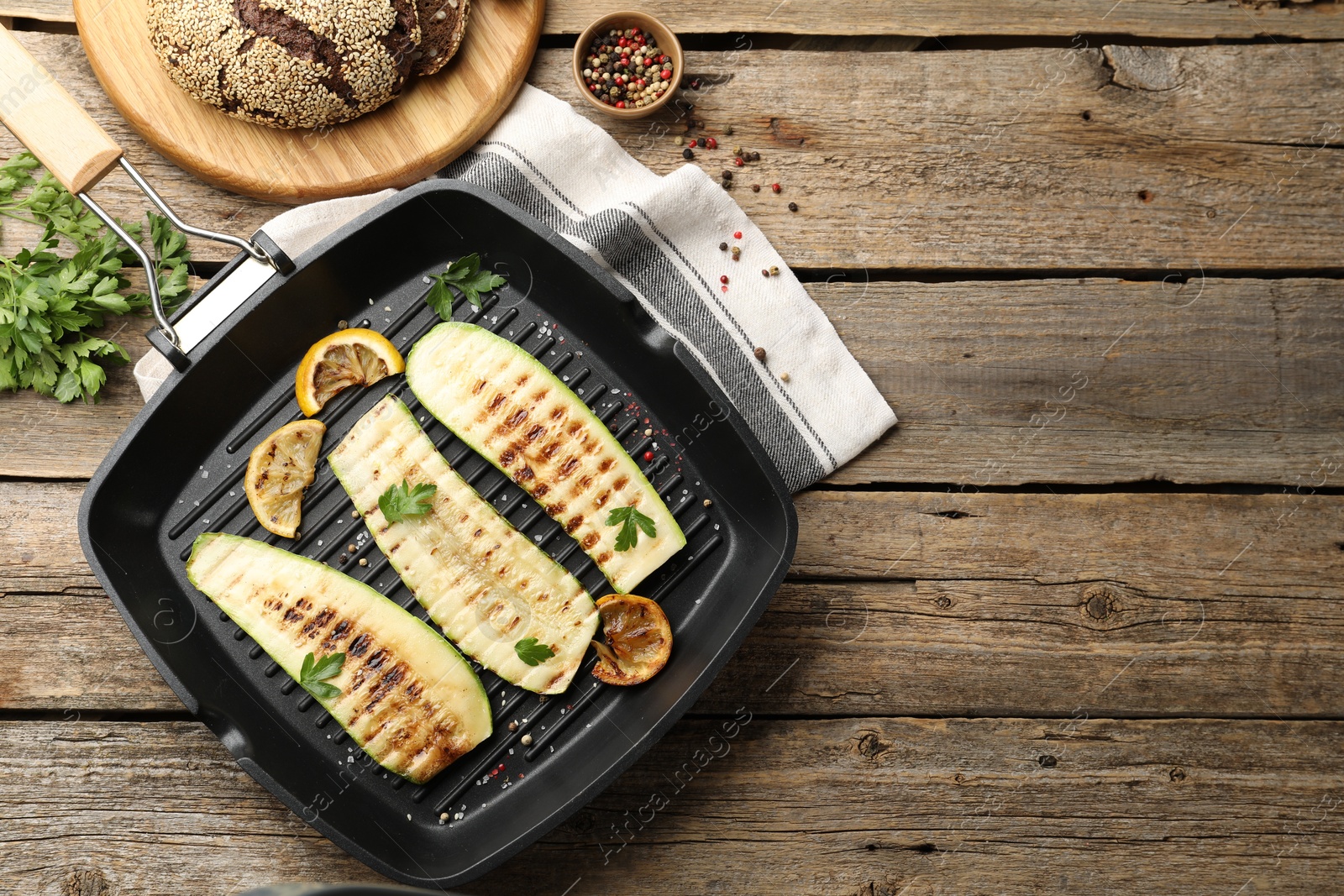 Photo of Delicious grilled courgette slices with spices and lemon in pan on wooden table, flat lay. Space for text