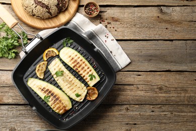 Photo of Delicious grilled courgette slices with spices and lemon in pan on wooden table, flat lay. Space for text